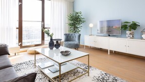 A modern living room with a glass coffee table, a grey sofa, a white cabinet, and a television on a stand. - Attractive Apartment in Den Haag with Balcony near Beach (The Hague)