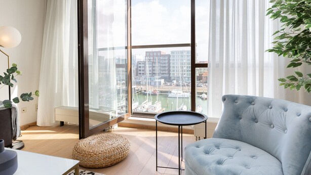 A modern living room with a large sliding glass door leading to a balcony with a marina view. - Attractive Apartment in Den Haag with Balcony near Beach (The Hague)