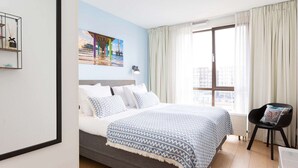 A hotel room with a bed, a chair, a window with curtains, and a wall with a picture. - Attractive Apartment in Den Haag with Balcony near Beach (The Hague)