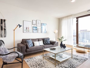 Una sala de estar moderna con un sofá gris, una mesa de centro de cristal y un tapete con estampado blanco y negro.
