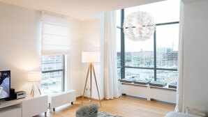 Un salon moderne avec une grande fenêtre, un lampadaire, un téléviseur et une plante décorative.