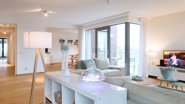 Un salon moderne avec un canapé blanc, une table basse en verre et un téléviseur posé sur un meuble.
