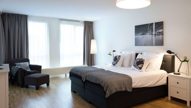 Une chambre moderne avec un grand lit, une chaise, un bureau et une lampe.