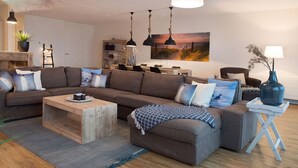 Un salon moderne avec un canapé d’angle, une table basse en bois et des luminaires suspendus.