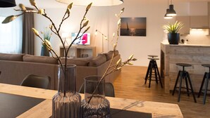 Un salon moderne avec un canapé, une table à manger agrémentée de vases et, au fond, un espace cuisine.