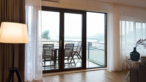 Une chambre d’hôtel moderne dotée d’une grande porte-fenêtre coulissante donnant sur un balcon, d’un canapé, d’une petite table et d’une lampe.
