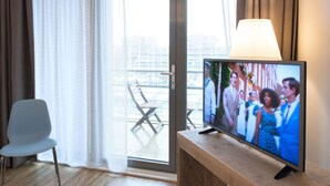 Une chambre d’hôtel avec une télévision posée sur une table en bois, une chaise grise et une porte-fenêtre coulissante donnant sur un espace extérieur.