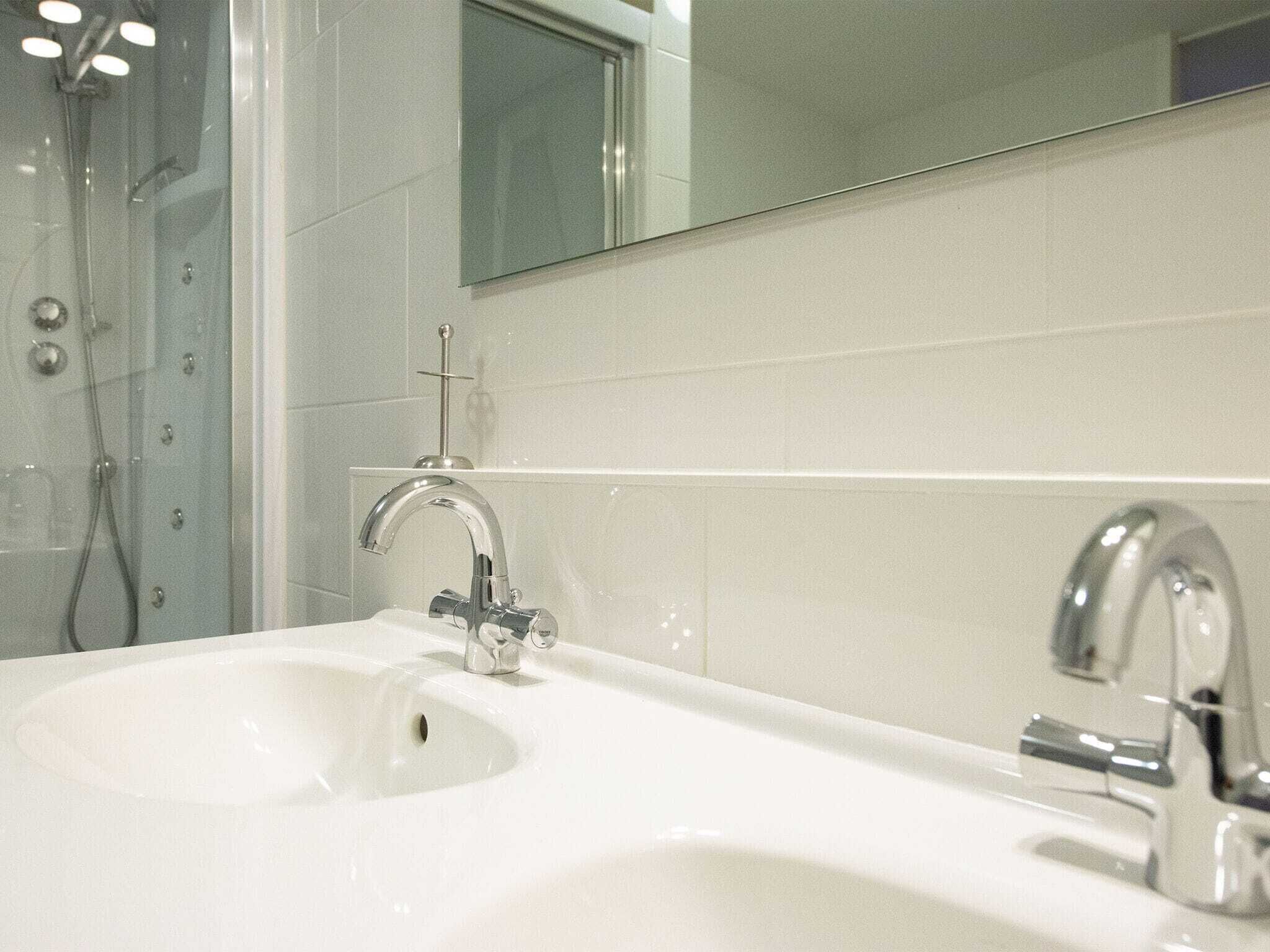 A bathroom with a white sink, two faucets, and a shower area with a glass door.