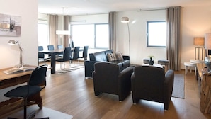 A modern living room with a sofa, chairs, a dining table, and a desk with a lamp. - Luxury Apartment in Scheveningen Harbor (The Hague)