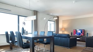 A modern hotel room with a dining area, a sofa, a television, and a large window. - Luxury Apartment in Scheveningen Harbor (The Hague)