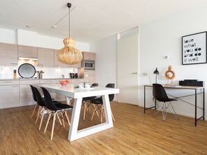 A modern kitchen with white cabinetry, a wooden dining table with black chairs, and a hanging light fixture. - Apartment in Netherlands With Marina View (The Hague)