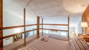 Quarto com teto de madeira, cama com roupa de cama listrada, mesa de cabeceira e abajur.