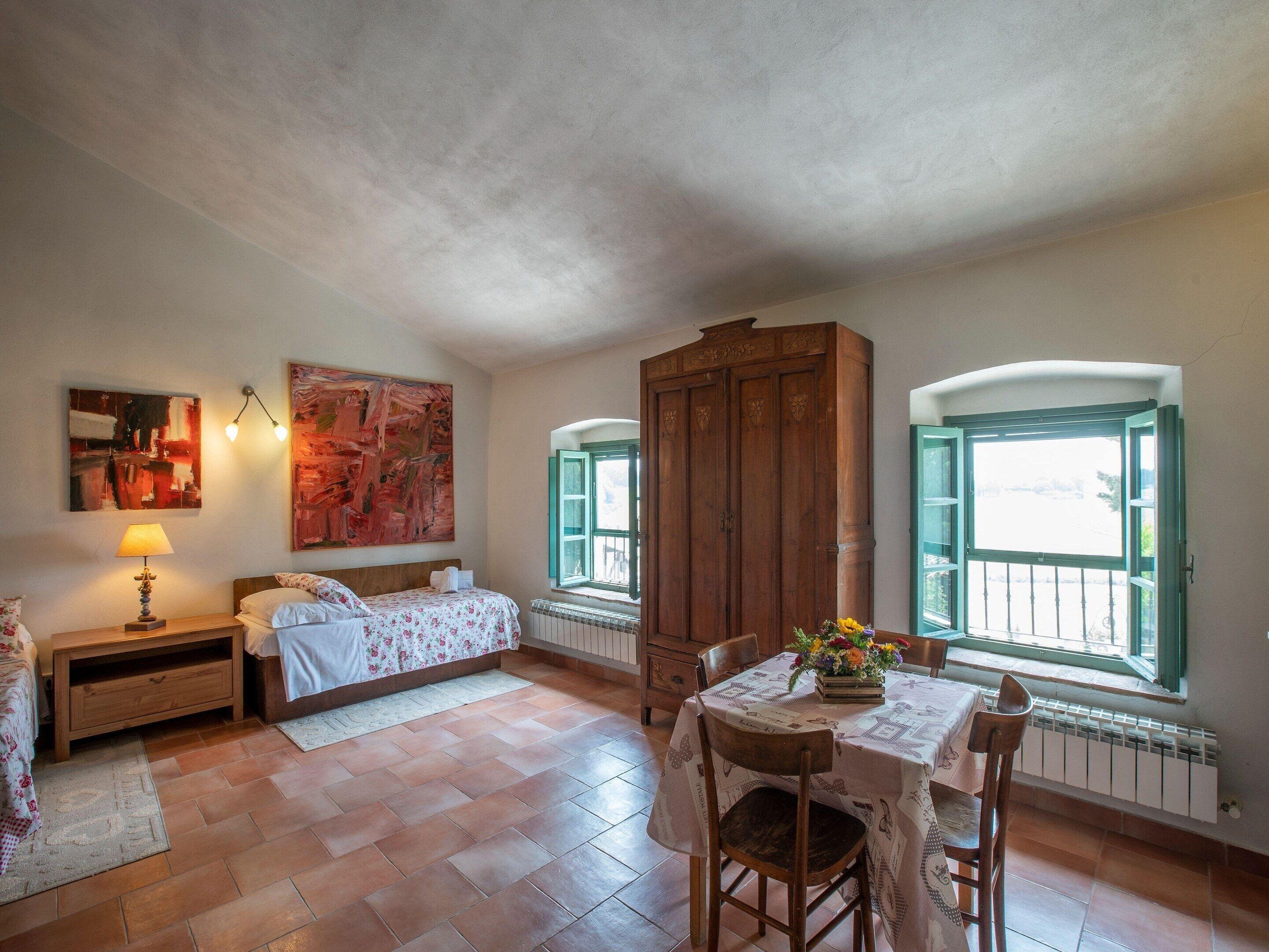 A bedroom with a bed, a nightstand, a dresser, a table with chairs, and a window with a view.