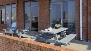 Une terrasse avec une table et des chaises, un mur en briques et de grandes fenêtres.
