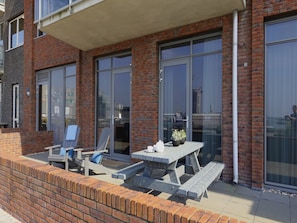 Un espace patio avec une table et des chaises, un mur en briques et de grandes fenêtres.