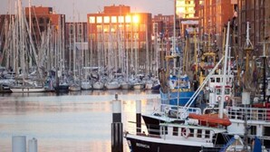Un port de plaisance où sont amarrés de nombreux bateaux, un bâtiment dont les fenêtres sont illuminées et un ciel dégagé.