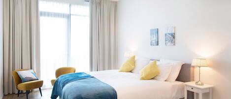 A hotel room with a large bed, two bedside lamps, a chair, and a window with curtains.