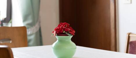 A table with a green vase containing red flowers, a wooden chair, and a white tablecloth.