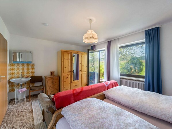 Un dormitorio con dos camas, un armario de madera, un escritorio pequeño con espejo y una ventana con cortinas.