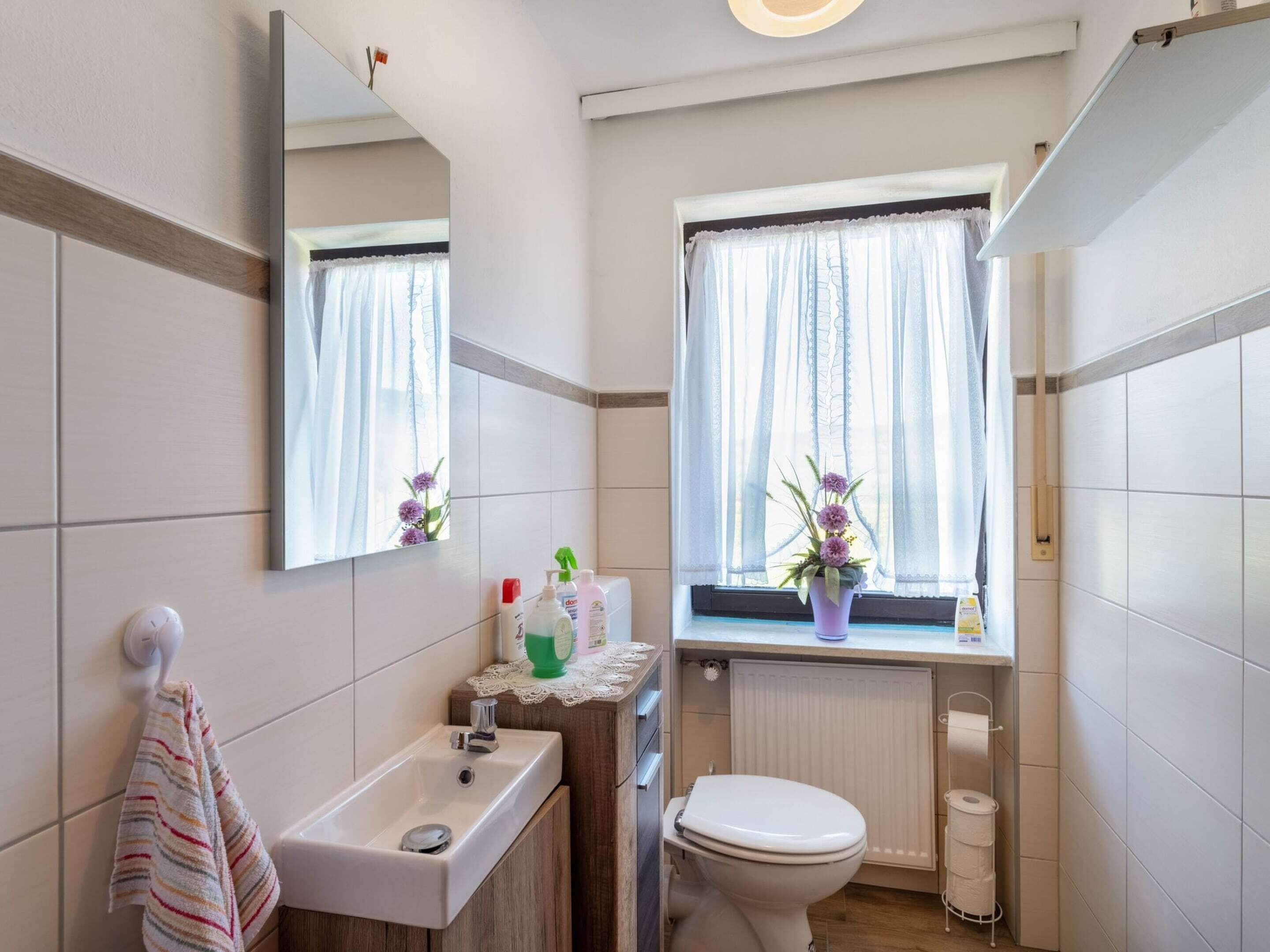 Une salle de bain équipée d’un lavabo, d’un miroir, de toilettes et d’une fenêtre avec des rideaux.