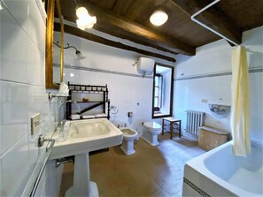 Un baño con lavamanos, inodoro y bañera. Hay una ventana con vistas al exterior.
