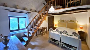 Un dormitorio con escalera de madera, cama con colcha floral, ventana con cortinas y radiador.