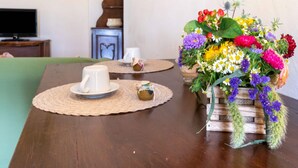 A wooden table with a woven placemat, a white mug, a small jar, and a vibrant floral arrangement in a wooden crate.