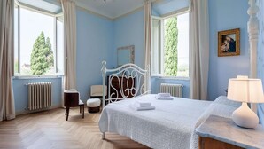 A bedroom with a bed, a chair, a nightstand, a lamp, and a window with curtains. - Holiday Home in Toscana With Pool (Larciano)
