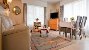 Un salon comprenant un canapé, un téléviseur, une table à manger avec des chaises et un tapis à motifs.
