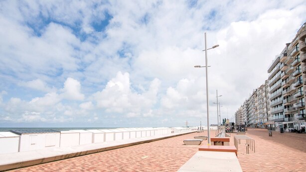 Une promenade en bord de mer bordée d’une rangée de bâtiments blancs, avec un chemin piétonnier pavé et un ciel dégagé.