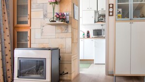 Un salon avec une cheminée, une horloge et un coin cuisine visible à travers une porte ouverte.