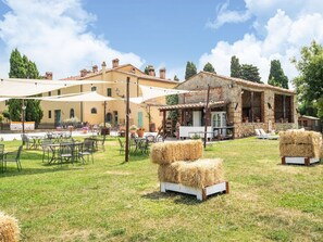 An outdoor seating area with tables and chairs, hay bales, and a building with stone walls and a tiled roof. - Apartment in Collesalvetti Near Pisa (Collesalvetti)