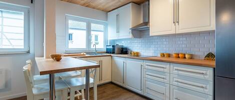 Una cocina moderna con armarios blancos, encimera de madera y refrigerador de acero inoxidable.