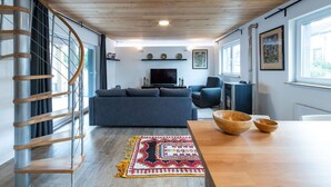 Una sala moderna con una escalera espiral, un conjunto de sofás, una mesa de comedor de madera y un ventanal grande.