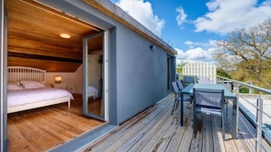 Un dormitorio moderno con techo de madera, una cama y un ventanal de vidrio que da a un balcón con mesa y sillas.
