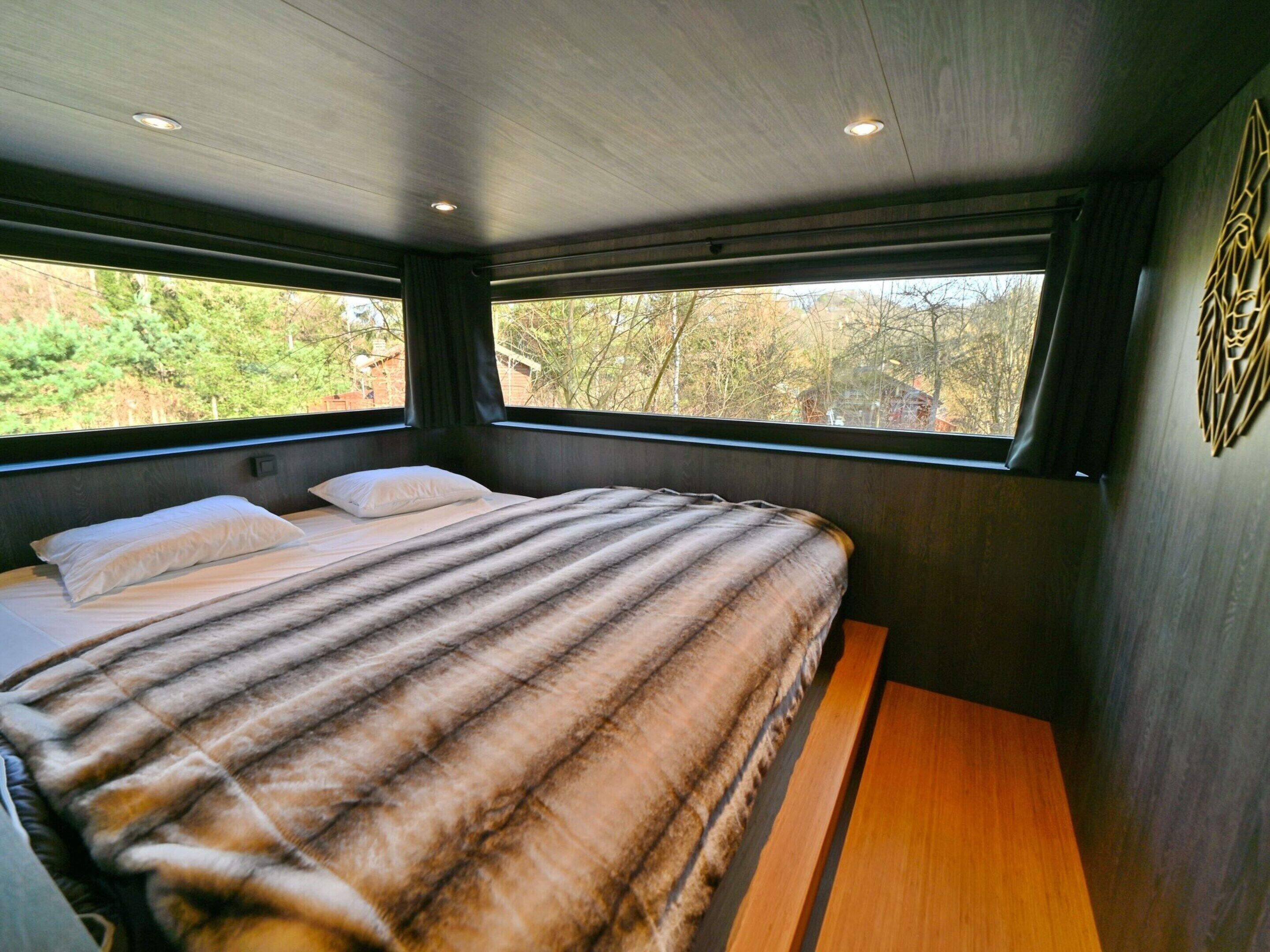 A bedroom with a bed, two windows, and a view of trees.