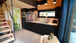 A modern kitchen with a wooden staircase, black cabinets, stainless steel appliances, and a window with a view. - Ecological Holiday Home near Durbuy with Nordic Bath (Durbuy)