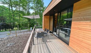 Une terrasse en bois avec des sièges extérieurs, entourée d’une zone boisée.