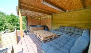 Un espace extérieur aménagé, abrité, avec un jacuzzi, une terrasse en bois et un grand canapé confortable.