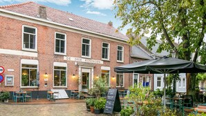 A brick building with a sign reading "DE DRIE KONINGEN" and outdoor seating with umbrellas. - Modern Holiday Home in Groede With a Terrace (Groede)