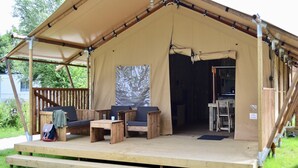 Een tent met een houten terras, een bank, een tafel en een stoel.