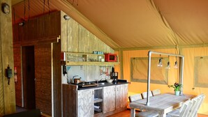 Een tentaccommodatie met houten inrichting, een keuken met fornuis en magnetron, een eettafel met stoelen, en een hanglamp.