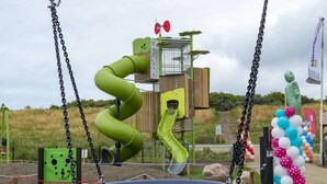 Een speeltuin met een groene spiraalglijbaan, een schommel en een decoratieve boog.