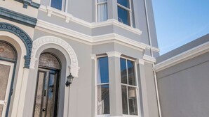 Esquina de un edificio con ventanal saliente, puerta con arco y molduras blancas alrededor de las ventanas.