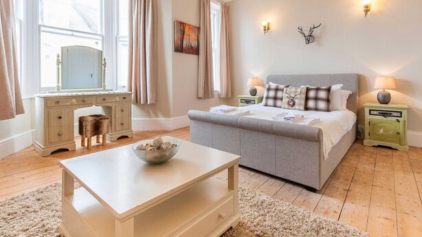 Un dormitorio con cama, mesitas de noche, cómoda, escritorio y ventana con cortinas.