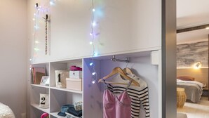 A bedroom with a bed, a bedside table, and a wardrobe with hanging clothes and shelves.