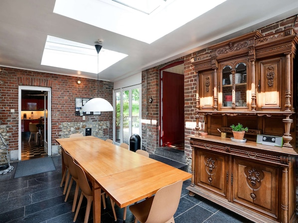 A spacious dining area with a long wooden table and chairs, a brick wall, and a large wooden cabinet with glass doors.