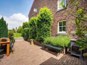 Een bakstenen huis met een patio, voorzien van een tafel, stoelen, een bank en een barbecue.