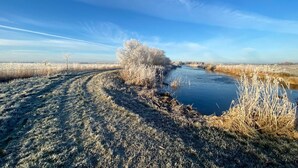Een door vorst bedekt landschap met een rivier, een heldere lucht en een pad dat door het beeld loopt.