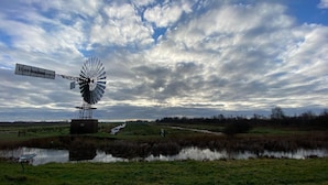 Een windmolen in een landelijk landschap onder een bewolkte lucht.